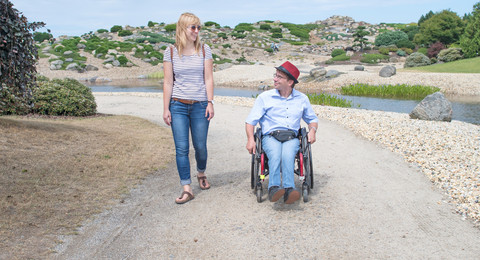Frau und Mann im Rollstuhl spazieren durch den Findlingspark
