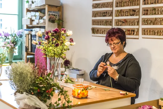 Blüten, die nie verwelken: Mit Fingerfertigkeit bewahren die sogenannten "Blümelfrauen" in der Deutschen Kunstblume Sebnitz ein beinahe ausgestorbenes Handwerk. Foto: Anna Meurer Eine Frau sitzt an einem Tisch und stellt eine Seidenrose her