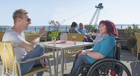Rollstuhlfahrerin mit Begleitung sitzen gemütlich im Café an den IBA-Terrassen