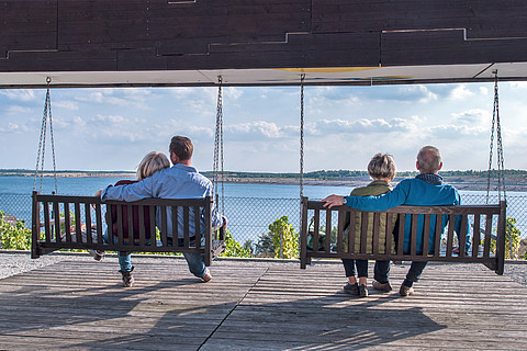 Besucher sitzen auf Schaukeln vor dem Großräschener See