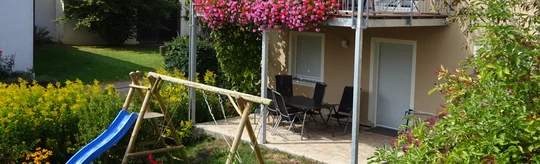 Gartenansicht mit Rutsche und Schaukel auf das Ferienhaus Wimbauer mit blühendem Balkon