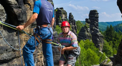 ein Kletterer wird gesichert beim Abseilen am Sandsteinfelsen