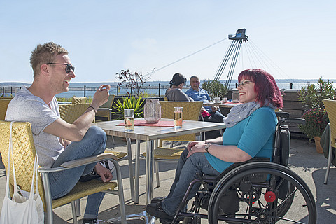 Rollstuhlfahrerin mit Begleitung sitzen gemütlich im Café an den IBA-Terrassen