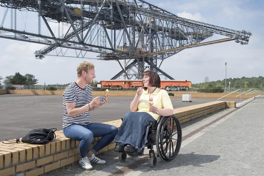Mann und Frau im Rollstuhl essen Eis am Fuße des Besucherbergwerks F60